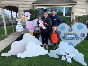 Family Posing with Stork Lawn Sign and baby